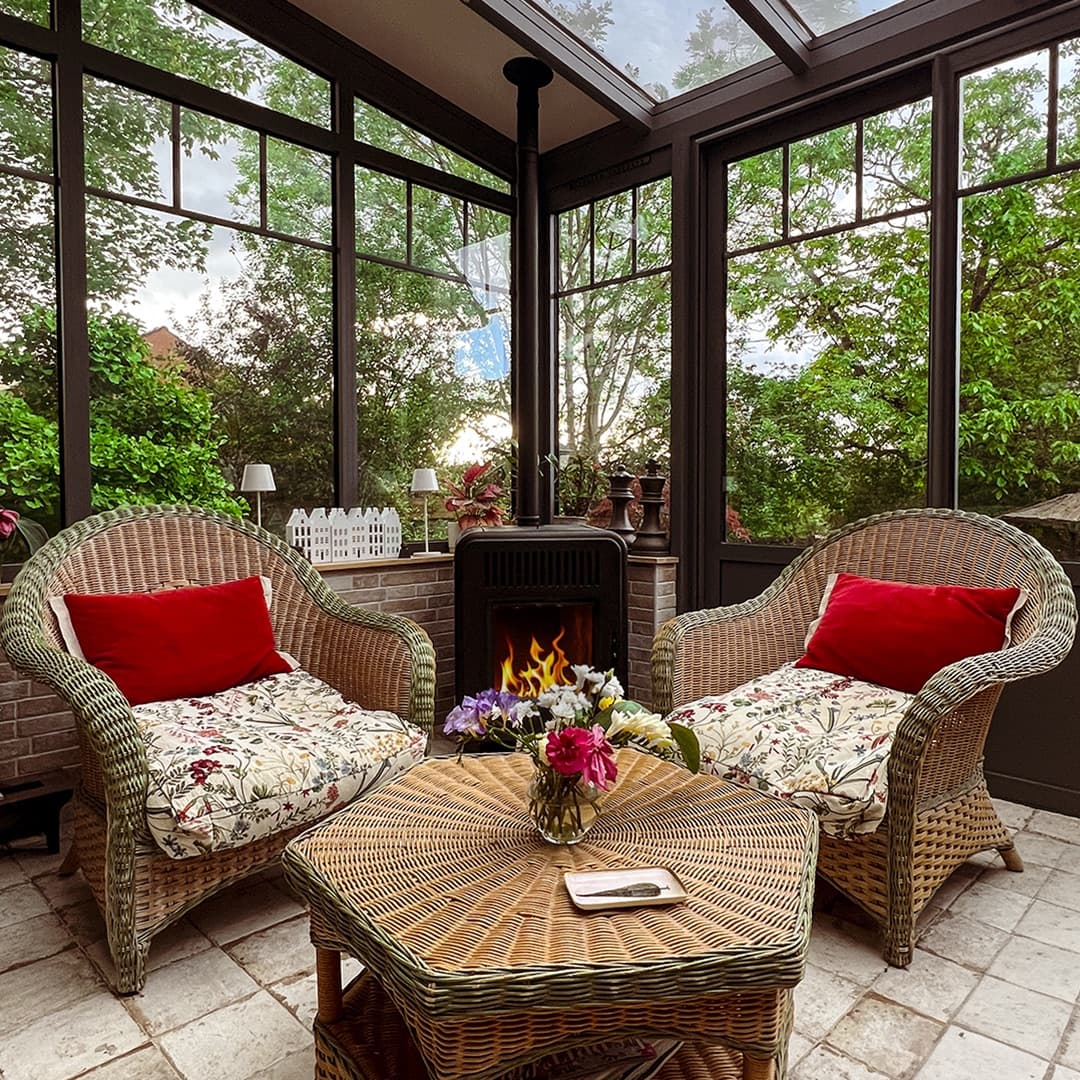Intérieur de la véranda aménagé en jardin d'hiver, mobilier en osier des années 30, Fontainebleau par Studio Songe